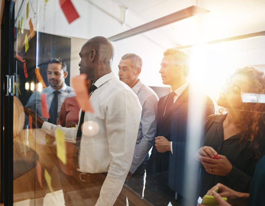 Young African businessman and his team brainstorming with sticky notes on a glass wall while working together in a modern office